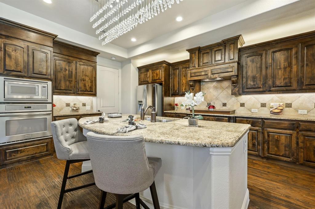 6705 Sigma Lane Frisco, TX 75035 - Photo 5 of 8 Gourmet kitchen featuring a substantial island with stone countertops, abundant dark wood cabinetry, a stainless steel built-in microwave and oven, and wood-finish flooring