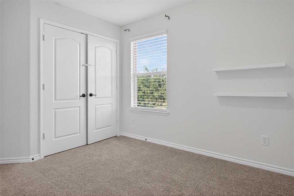 8728 Maple Ridge Trail Fort Worth, TX 76244 - Photo 30 of 40 White interior walls with neutral carpet flooring, featuring double panel doors with matte black hardware, a window with blinds, and two wall-mounted shelves