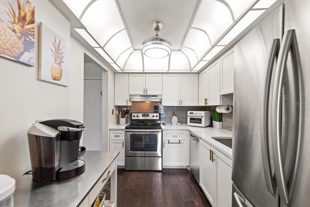 255 Dolphin Point, Unit 508 Clearwater Beach, FL 33767 - Photo 19 of 40 a kitchen with stainless steel appliances a stove a sink dishwasher a refrigerator white cabinets and wooden floor