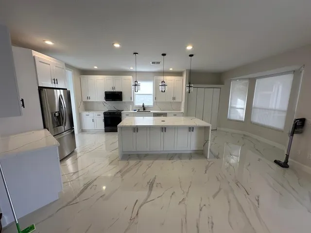 a living room with stainless steel appliances furniture a fireplace a flat screen tv and a kitchen view