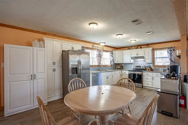 a kitchen with stainless steel appliances granite countertop a refrigerator a stove top oven a sink dishwasher and white cabinets with wooden floor