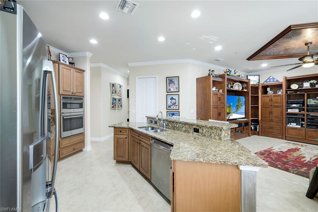 11050 Longwing Drive Fort Myers, FL 33912 - Photo 8 of 43 Kitchen with stainless steel appliances, a kitchen island with sink, crown molding, light stone counters, and a ceiling fan