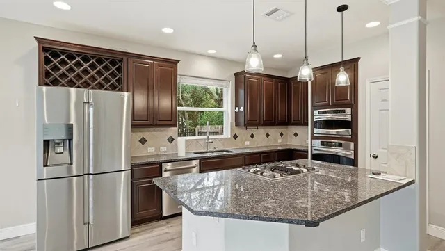 a kitchen with stainless steel appliances granite countertop a refrigerator a oven and a sink with wooden floor