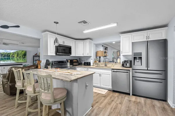 a kitchen with stainless steel appliances granite countertop a refrigerator a stove top oven a sink dishwasher and white cabinets with wooden floor