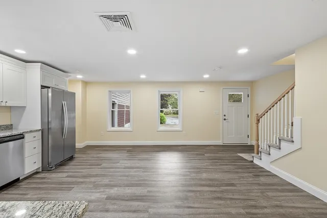 a view of an empty room with wooden floor and a kitchen