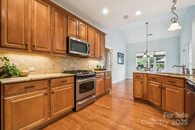 a kitchen with stainless steel appliances granite countertop wooden cabinets a stove a sink and dishwasher with wooden floor