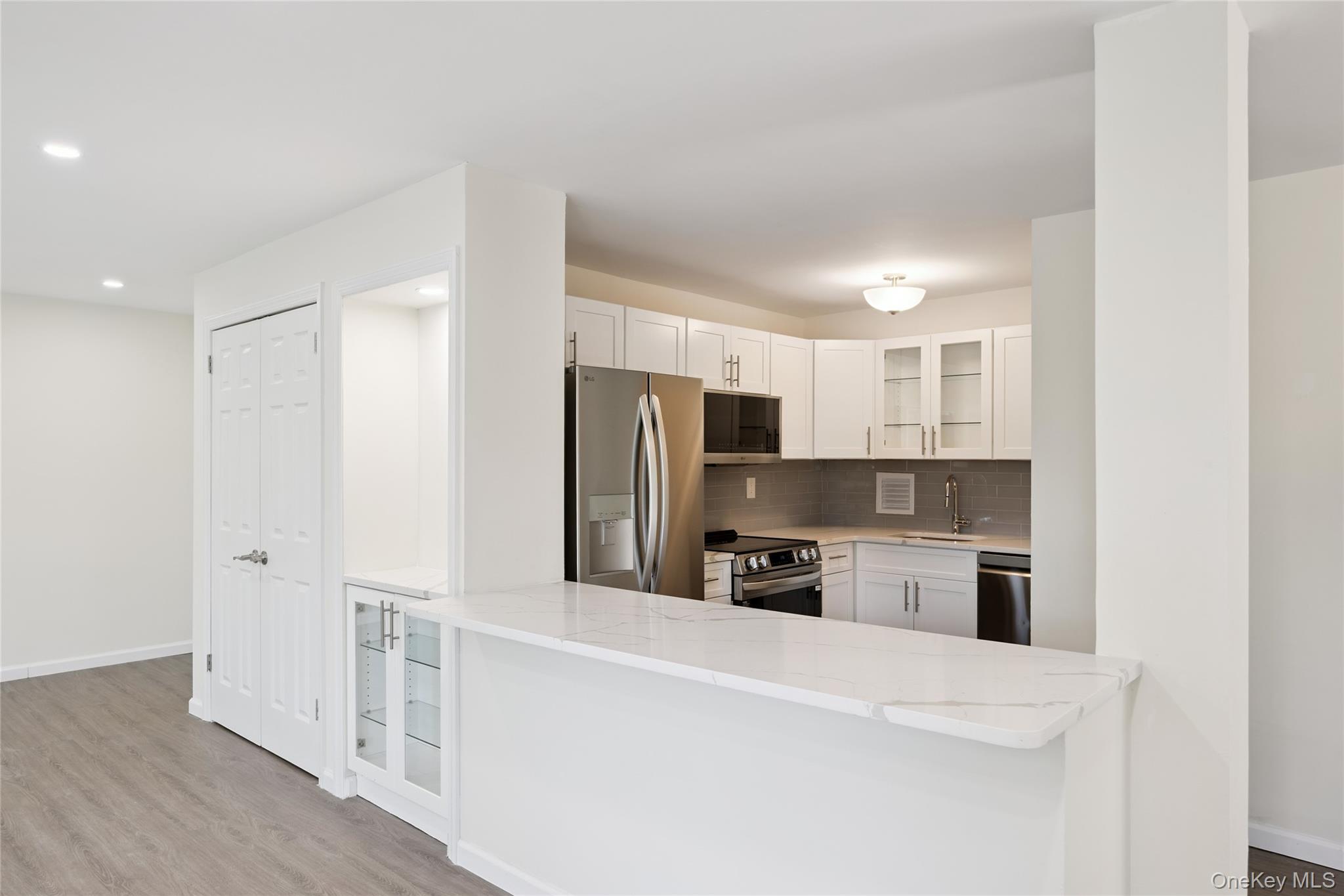 7-04 166th Street, Unit 6A Queens, NY 11357 - Photo 1 of 1 Kitchen with glass insert cabinets, appliances with stainless steel finishes, light wood-style floors, tasteful backsplash, and light stone counters