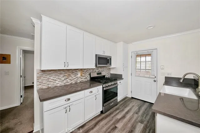 a kitchen with granite countertop a sink dishwasher stove and white cabinets with wooden floor