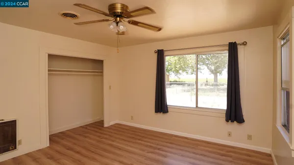 an empty room with wooden floor fan and windows