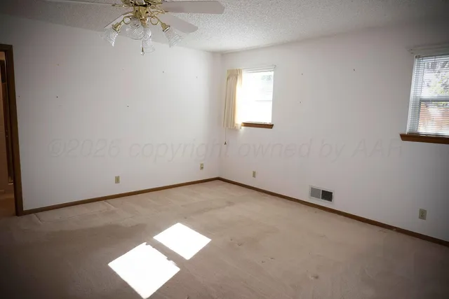 an empty room with chandelier fan and windows