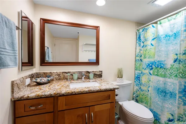 a bathroom with a granite countertop toilet a sink and a mirror