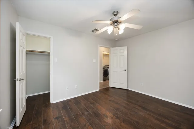 a view of an empty room with wooden floor and a ceiling fan