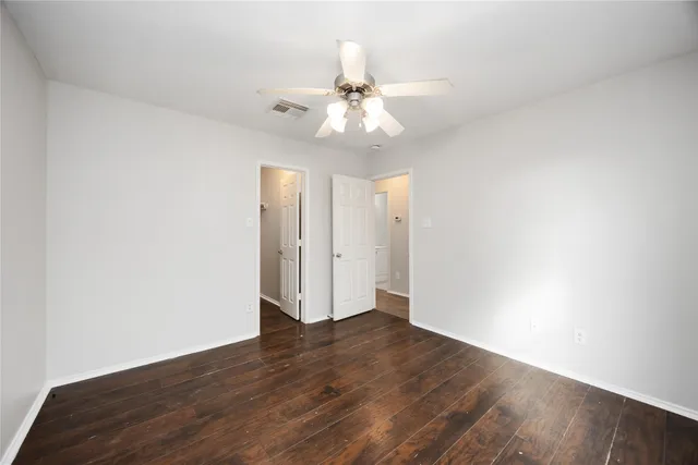 a view of an empty room with wooden floor and a ceiling fan