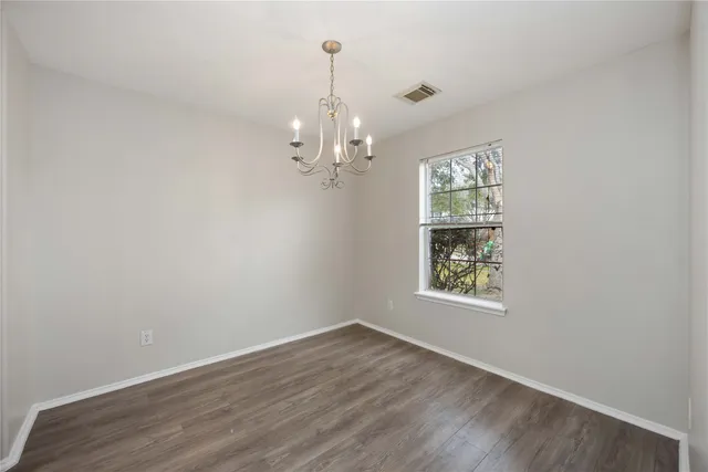 an empty room with wooden floor chandelier and windows