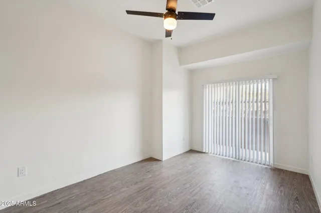 an empty room with wooden floor fan and windows