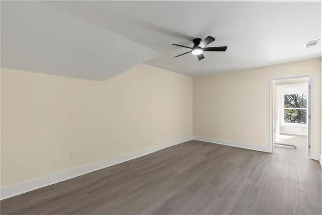 an empty room with wooden floor ceiling fan and windows
