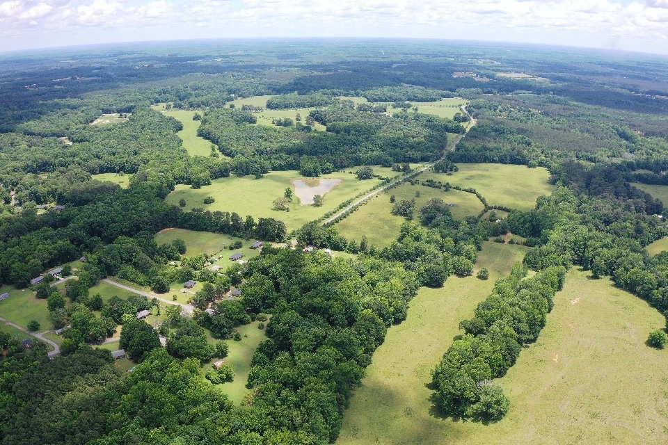 0 Cherokee Road Belton, SC 29627 - Photo 3 of 3 Vast green acreage unfolds with a winding road, scattered homes, and a tranquil pond, surrounded by lush woodlands.