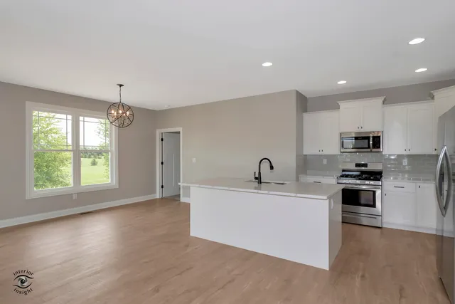 a kitchen with stainless steel appliances a sink a stove a refrigerator cabinets and a wooden floor