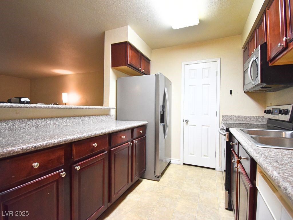 2451 North Rainbow Boulevard, Unit 1130 Las Vegas, NV 89108 - Photo 9 of 21 Kitchen featuring reddish brown cabinets, stainless steel appliances, and light tile patterned floors