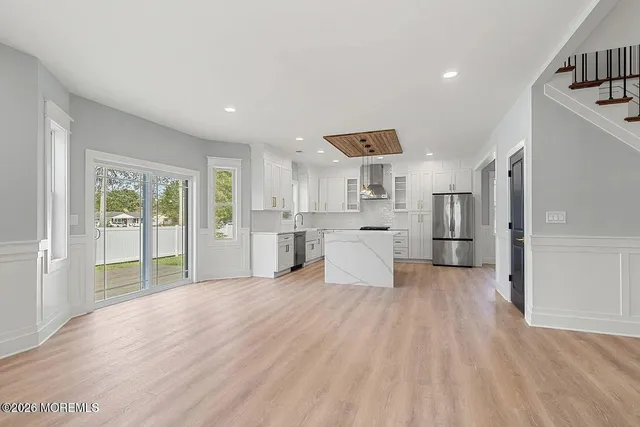 a large white kitchen with stainless steel appliances granite countertop a refrigerator oven sink and white cabinets with wooden floor