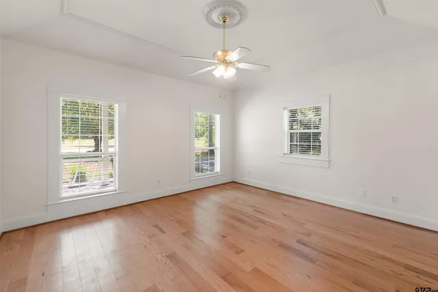an empty room with wooden floor chandelier fan and windows