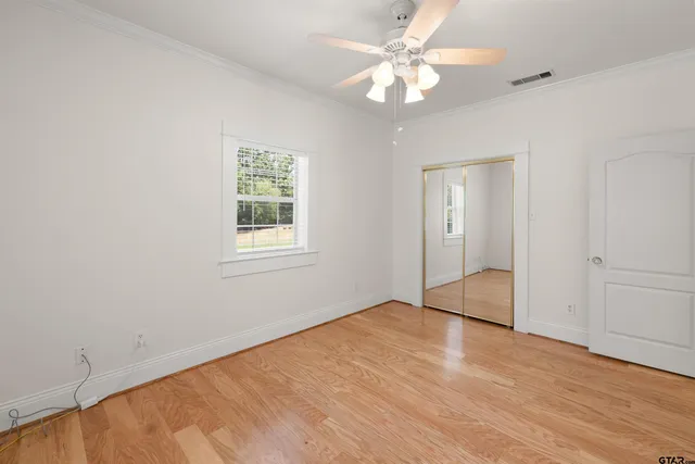 an empty room with wooden floor fan and windows