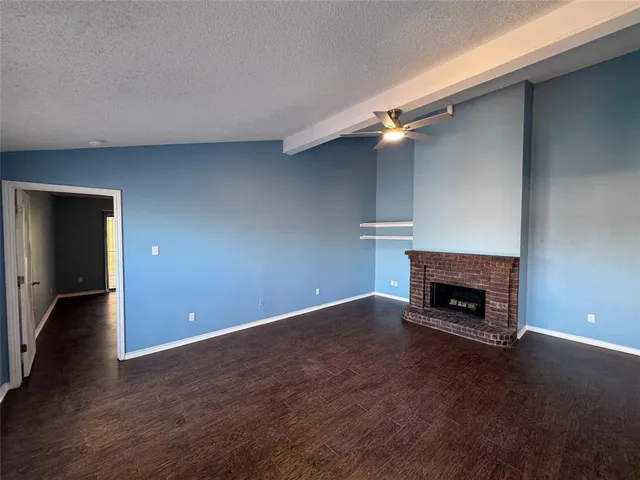 an empty room with wooden floor fireplace and windows