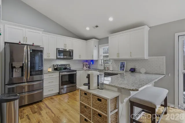 a kitchen with granite countertop a stove top oven a sink dishwasher a refrigerator and white cabinets with wooden floor