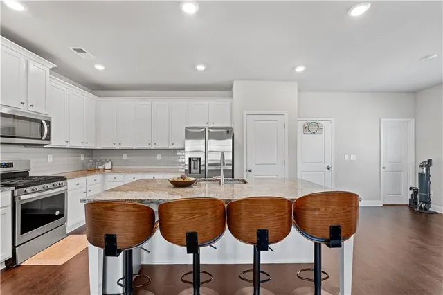 a kitchen with stainless steel appliances granite countertop a stove a sink a refrigerator and white cabinets with wooden floor