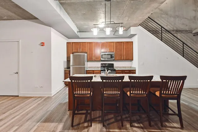 a kitchen with stainless steel appliances granite countertop a refrigerator a stove top oven a sink dishwasher a dining table and chairs with wooden floor