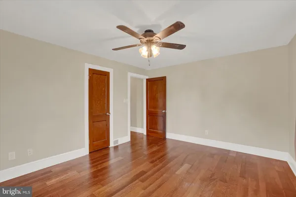 a view of an empty room with wooden floor and a ceiling fan