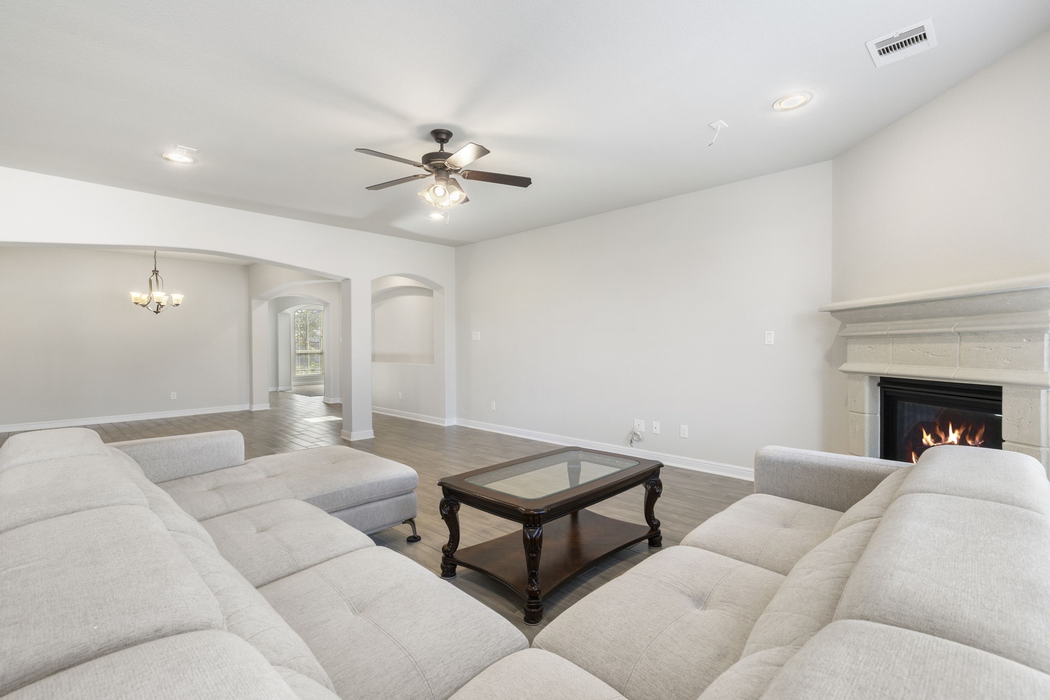 2819 Bradbury Hills Road Spring, TX 77373 - Photo 19 of 50 This spacious living area features an elegant fireplace, cozy sectional sofa, and a ceiling fan. It has an open layout with archways leading to additional spaces, complemented by wood flooring and neutral walls for a modern, inviting atmosphere.
