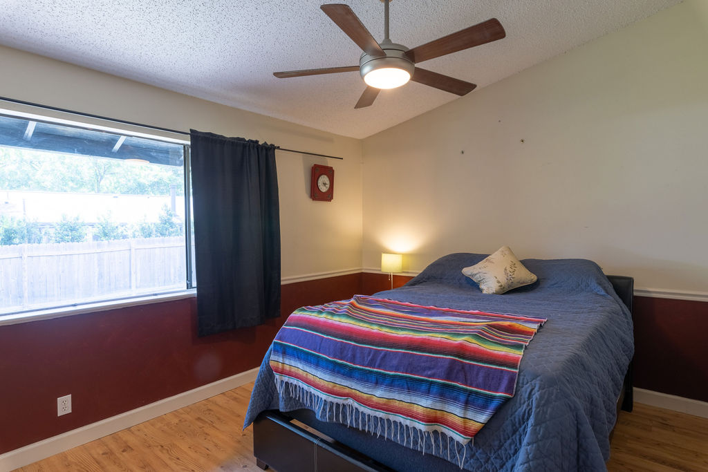 5310 Presidio Road Austin, TX 78745 - Photo 15 of 34 A comfortable bedroom features a wide window and natural wood flooring, complemented by an overhead fan for air circulation.