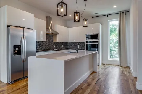 a kitchen with stainless steel appliances granite countertop a refrigerator a oven a sink and a wooden floor