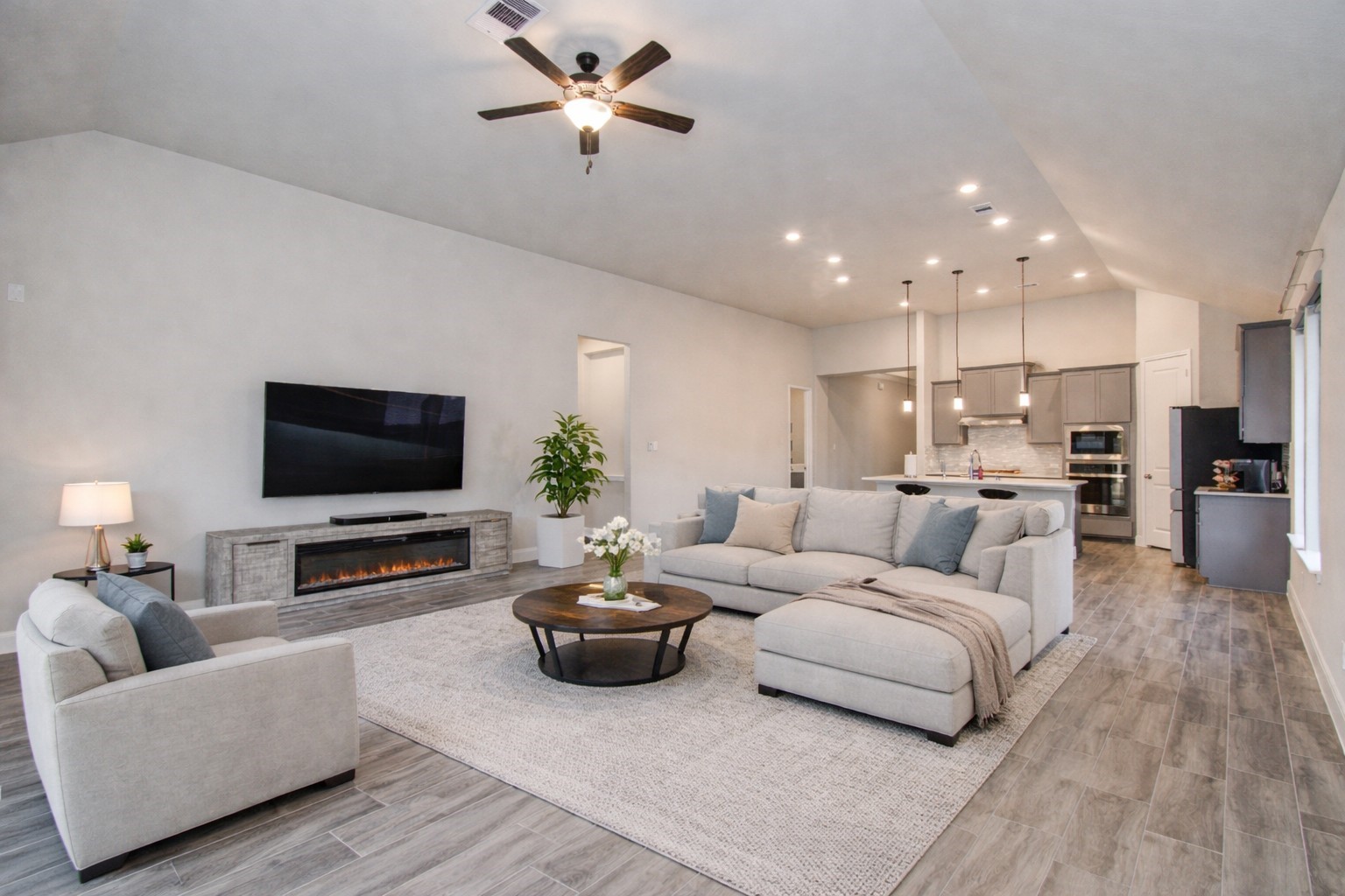 17344 Grand Canyon Road Conroe, TX 77302 - Photo 35 of 49 This open-concept living area features a spacious layout with a modern kitchen, cozy seating around a fireplace, and a large TV. The room is bright and inviting with stylish lighting and wood-look flooring.