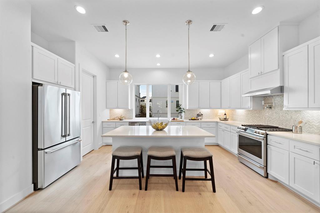 a kitchen with stainless steel appliances a stove a sink a refrigerator and white cabinets with wooden floor