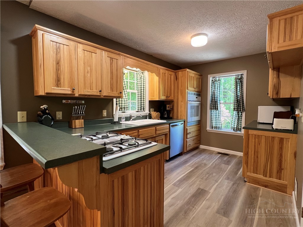 139 New River Ridge Estates Laurel Springs, NC 28644 - Photo 9 of 34 a kitchen with stainless steel appliances granite countertop a stove top oven a refrigerator a sink dishwasher with a dining table and chairs with wooden floor
