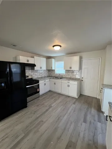 a large kitchen with a stove a sink dishwasher a refrigerator and white cabinets with wooden floor