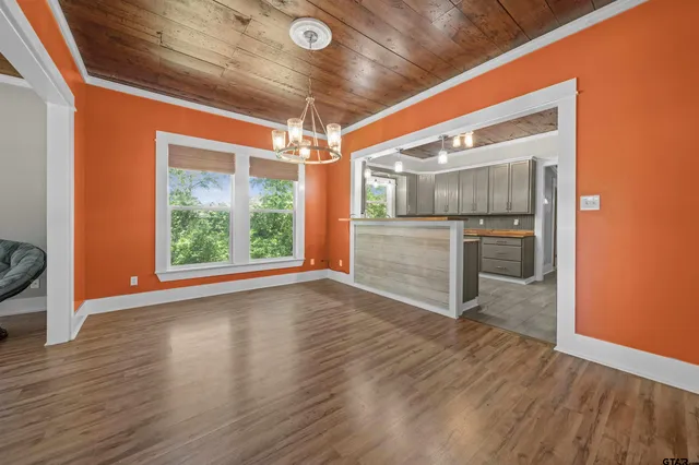 a view of an empty room with wooden floor kitchen view and a fireplace