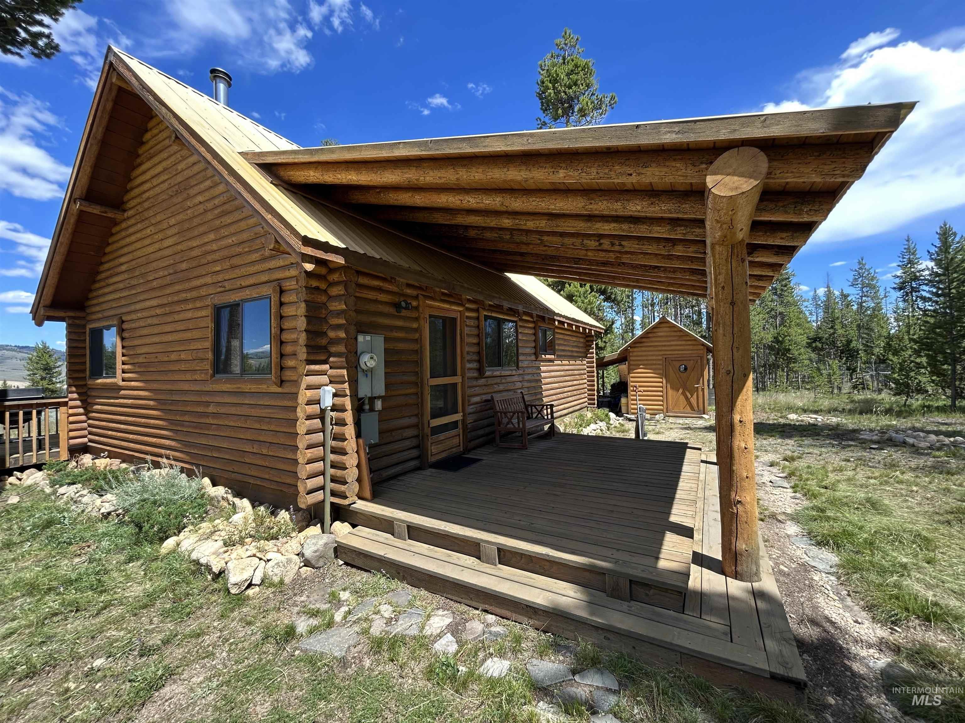 35 Sawtooth Way Stanley, ID 83278 - Photo 6 of 36 Rustic log cabin exterior featuring a covered porch, wood-finish decking, and a metal roof