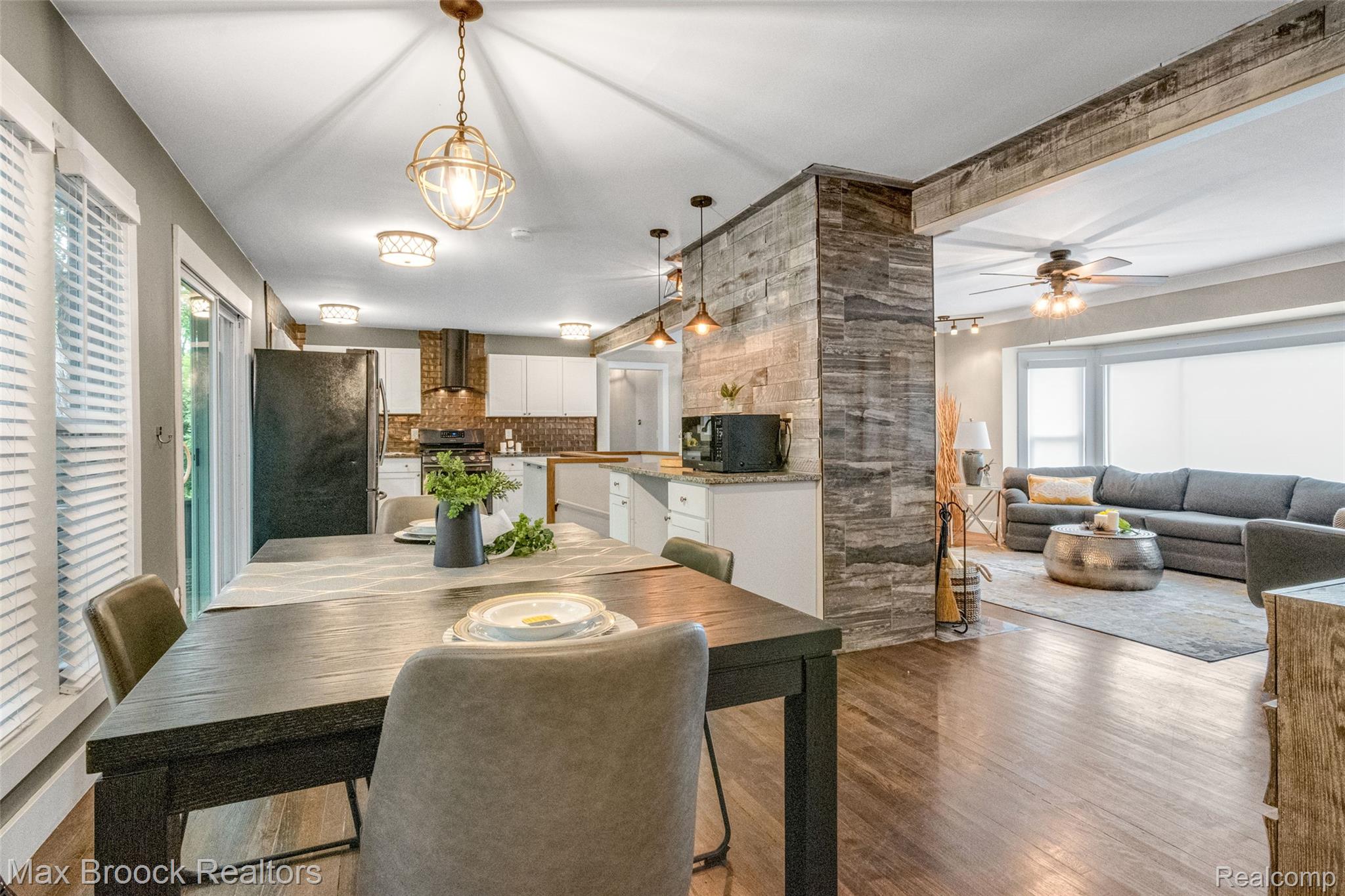 2905 Lahser Road Bloomfield Hills, MI 48304 - Photo 11 of 28 Open-concept interior featuring wood-finish flooring, a kitchen with white cabinetry and brick-patterned backsplash, and a dining area illuminated by a brass-finish pendant light