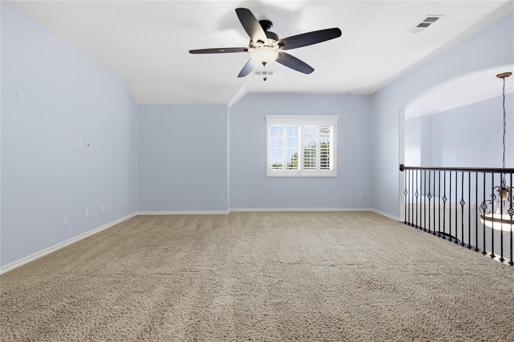 10001 Thurman Road Fort Worth, TX 76244 - Photo 28 of 40 Spacious carpeted room featuring a ceiling fan, a window with plantation shutters, an arched entryway, and an ornate metal railing