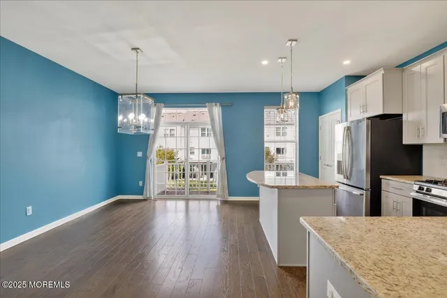 a kitchen with granite countertop a refrigerator a stove a sink and white cabinets with wooden floor