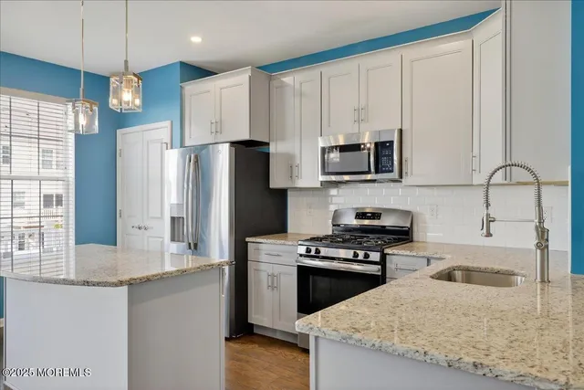 a kitchen with stainless steel appliances granite countertop a stove top oven a sink dishwasher and white cabinets with wooden floor