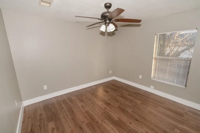 an empty room with wooden floor fan and windows