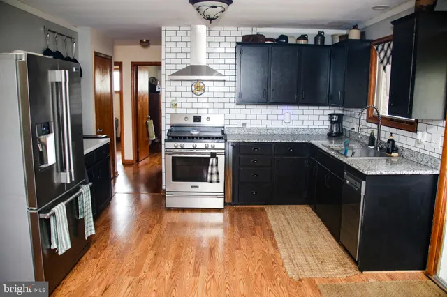 a kitchen with stainless steel appliances granite countertop a refrigerator a stove a sink and wooden cabinets with wooden floor