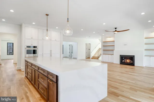 a large white kitchen with kitchen island a large island a stove a refrigerator cabinets and couches with wooden floor