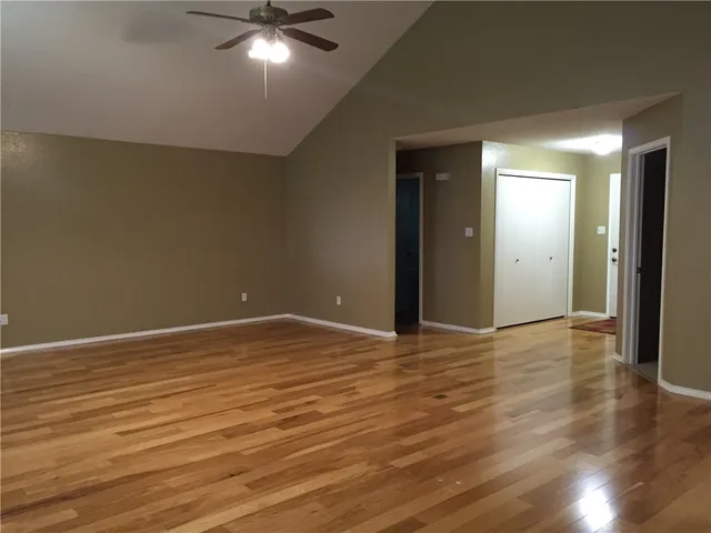 a view of an empty room with wooden floor and a ceiling fan