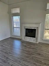 an empty room with wooden floor fire place and windows
