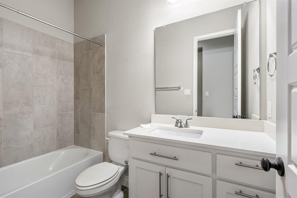 1501 Calcot Lane Forney, TX 75126 - Photo 24 of 34 Bathroom featuring a white vanity with a white countertop and integrated sink, a large frameless mirror, and a white bathtub with light gray tiled surround